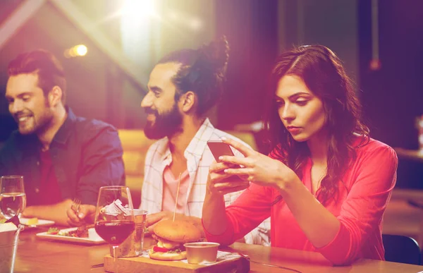 Mulher com smartphone e amigos no restaurante — Fotografia de Stock