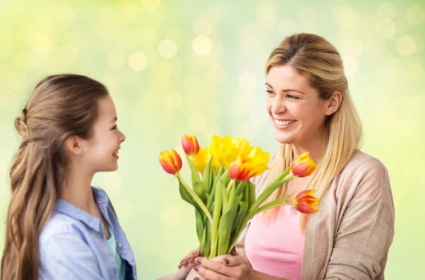 Happy girl giving flowers to mother over lights — Stock Photo, Image