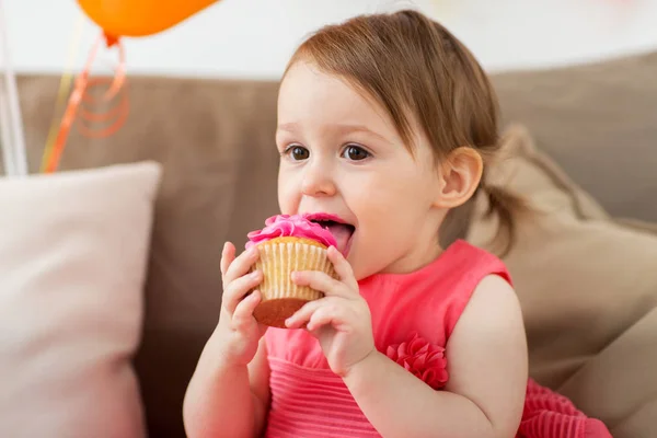 Happy baby girl eating cupcake on birthday party — Stock Photo, Image