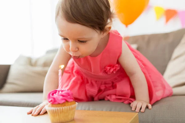 Menina soprando para vela no cupcake no aniversário — Fotografia de Stock