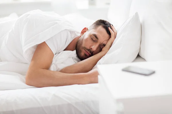 Hombre durmiendo en la cama con smartphone en la mesita de noche —  Fotos de Stock