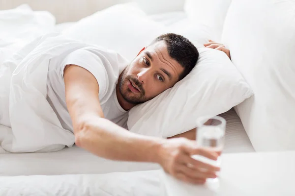 Hombre en la cama y llegar a un vaso de agua en casa —  Fotos de Stock