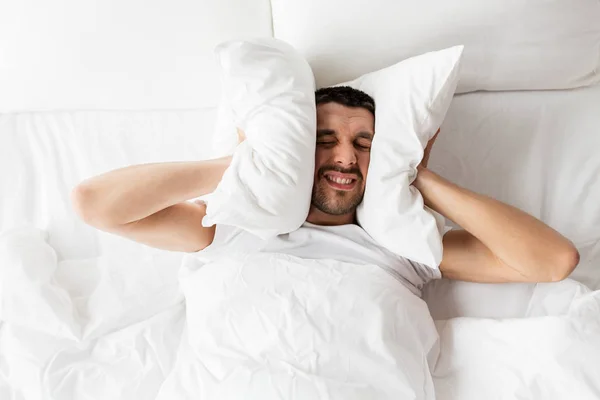 Hombre en la cama con almohada que sufre de ruido — Foto de Stock