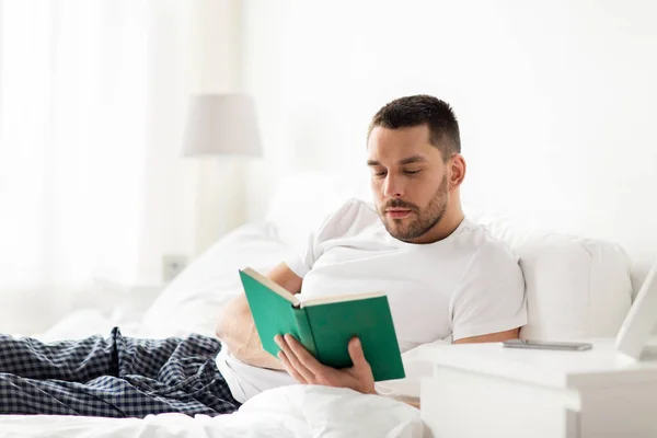 Homem lendo livro na cama em casa — Fotografia de Stock