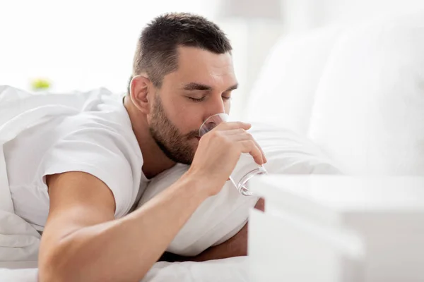 Man in bed with glass of water drinking at home — Stock Photo, Image