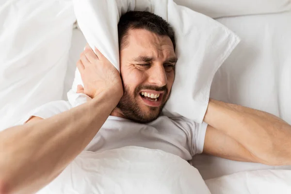 Hombre en la cama con almohada que sufre de ruido — Foto de Stock