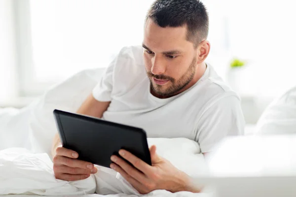 Hombre joven con tableta pc en la cama en el dormitorio en casa —  Fotos de Stock