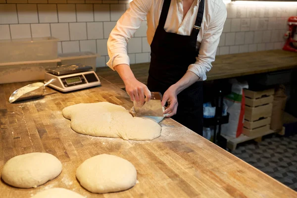 Baker portioning dough with bench cutter at bakery — Stock Photo, Image