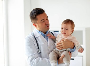 doctor holding crying baby at clinic clipart