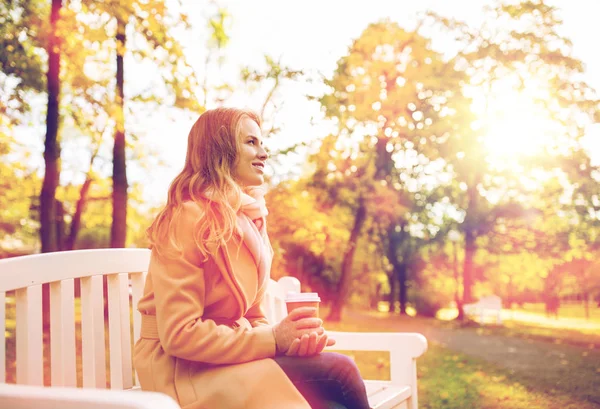 Happy young woman drinking coffee in autumn park — Stock Photo, Image