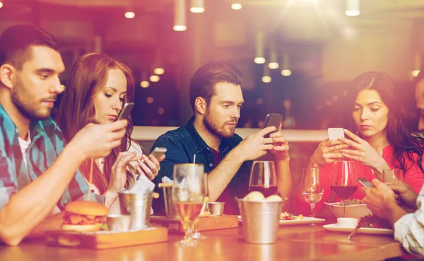 Amigos com smartphones jantando no restaurante — Fotografia de Stock