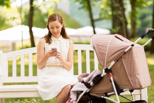 Happy mother with smartphone and stroller at park — Stock Photo, Image