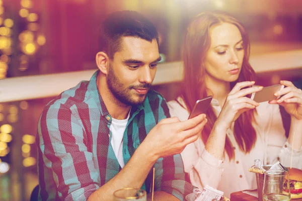 Paar mit Smartphones beim Essen im Restaurant — Stockfoto