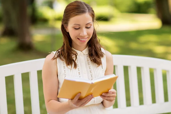 Jeune femme souriante lisant le livre au parc d'été — Photo