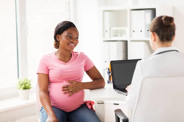 Médico con portátil y mujer embarazada en la clínica —  Fotos de Stock