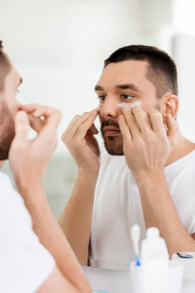 Young man applying cream to face at bathroom — Stock Photo, Image