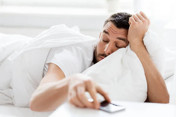 Jovem chegando para smartphone na cama — Fotografia de Stock