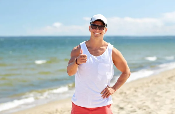 Uomo sorridente sulla spiaggia estiva mostrando pollici in su — Foto Stock