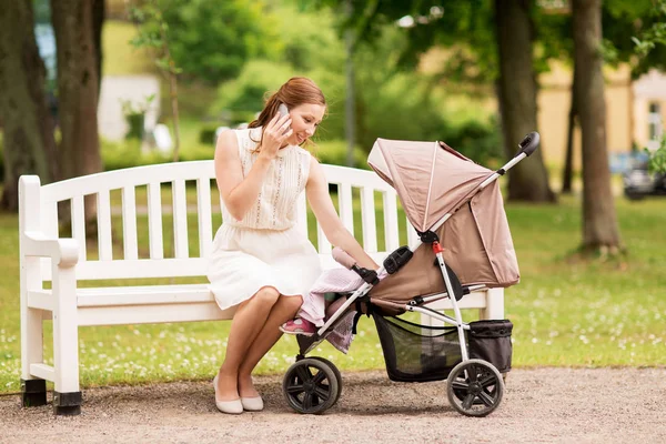 Madre feliz con smartphone y cochecito en el parque — Foto de Stock