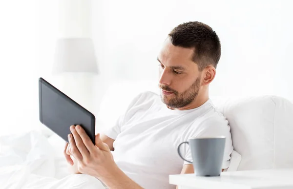 Mladý muž s tablet pc v posteli na domácí ložnice — Stock fotografie