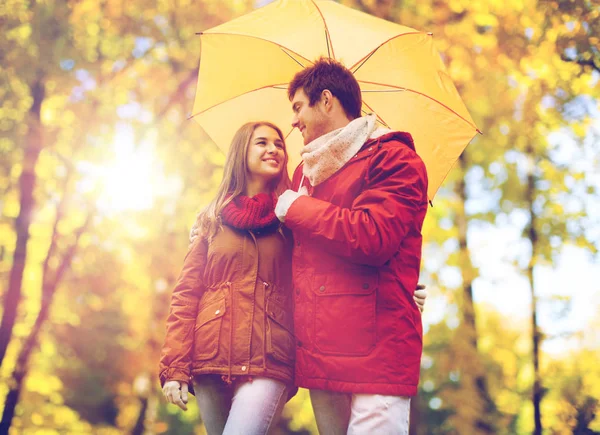 Coppia sorridente con ombrellone nel parco autunnale — Foto Stock