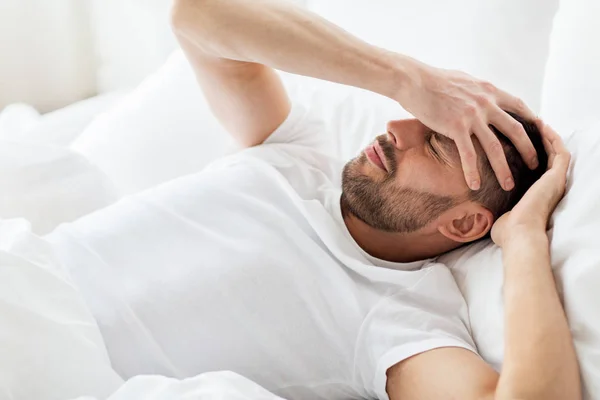 Hombre en la cama en casa sufriendo de dolor de cabeza —  Fotos de Stock