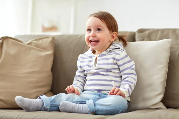 Lyckligt leende flicka sitter på soffan hemma — Stockfoto