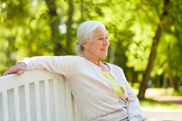 Счастливая пожилая женщина, сидящая на скамейке в летнем парке — стоковое фото