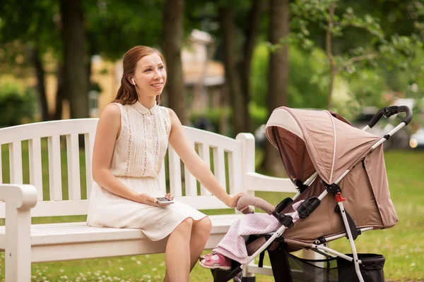Happy mother with smartphone and stroller at park — Stock Photo, Image