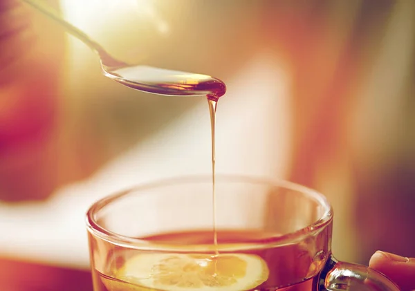 Close up of woman adding honey to tea with lemon — Stock Photo, Image