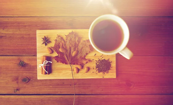 Taza de té, hoja de arce y almendra sobre tabla de madera — Foto de Stock