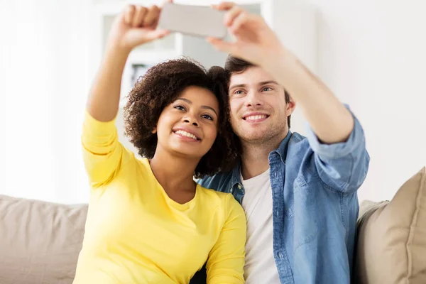 Casal feliz com smartphone levando selfie em casa — Fotografia de Stock