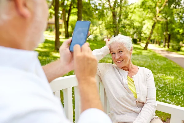 Homem velho fotografando mulher por smartphone no parque — Fotografia de Stock
