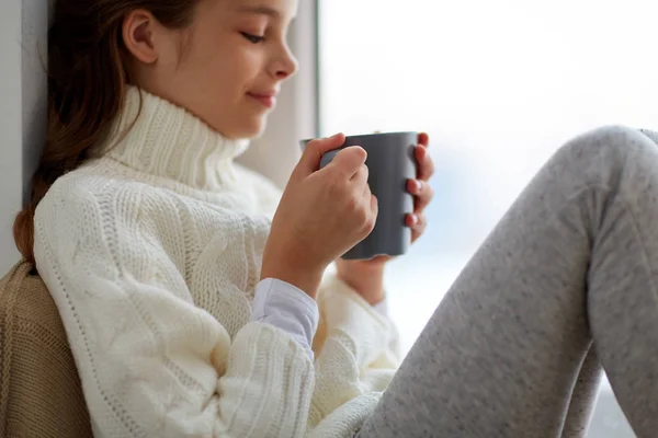 Flicka med te mugg sitter hemma fönster — Stockfoto
