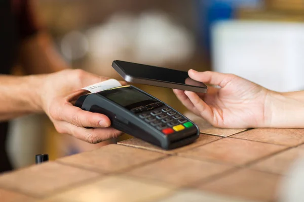 Hands with payment terminal and smartphone at bar — Stock Photo, Image