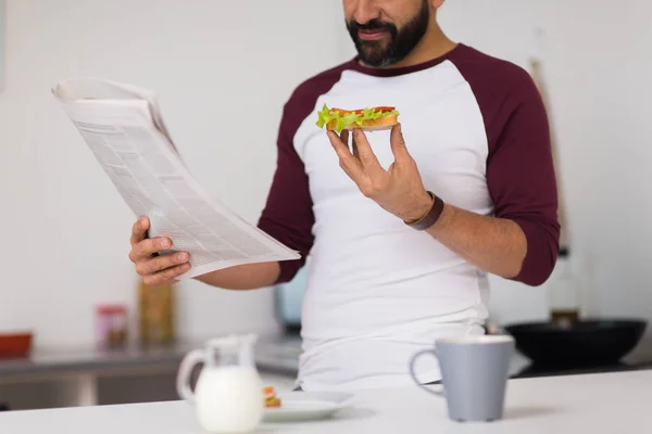 Мужчина читает газету и ест на домашней кухне — стоковое фото