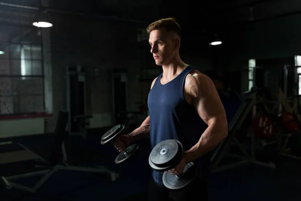 Young man with dumbbells exercising in gym — Stock Photo, Image