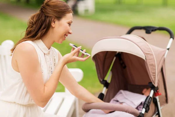Happy mother with smartphone and stroller at park — Stock Photo, Image