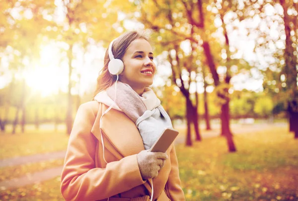 Woman with smartphone and earphones in autumn park — Stock Photo, Image