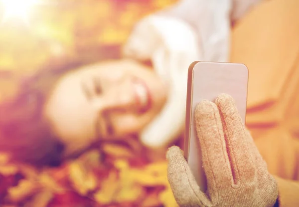 Woman on autumn leaves taking selfie by smartphone — Stock Photo, Image