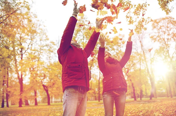 Feliz jovem casal jogando folhas de outono no parque — Fotografia de Stock