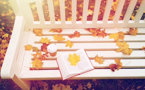 Открытая книга и чашка кофе на скамейке в осеннем парке — стоковое фото