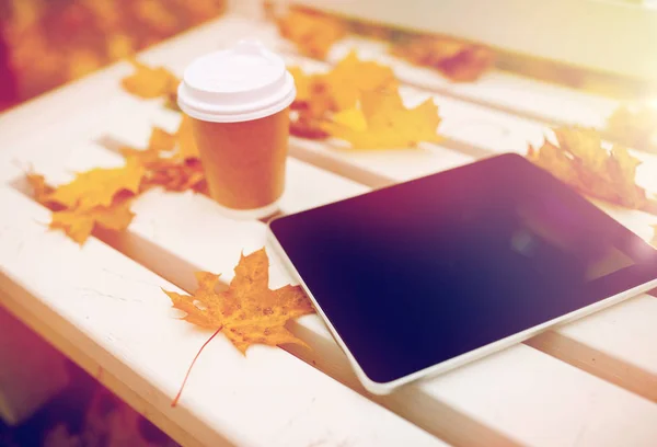 Tablet pc och kaffe kopp på bänk i höst park — Stockfoto