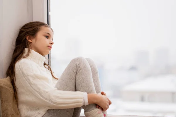 Triste fille assis sur le seuil à la fenêtre de la maison en hiver — Photo