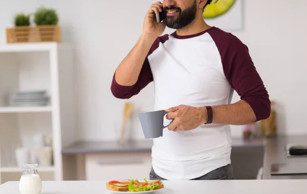 Hombre llamando en el teléfono inteligente y comer en casa — Foto de Stock