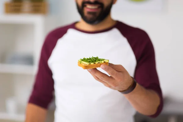 Pria makan sandwich alpukat di dapur rumah — Stok Foto