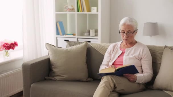 Senior Kvinna i glasögon bok hemma — Stockvideo