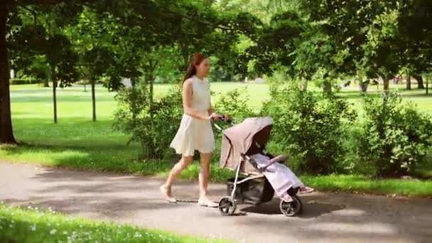 Gelukkig moeder met baby in kinderwagen, wandelen in het park — Stockvideo