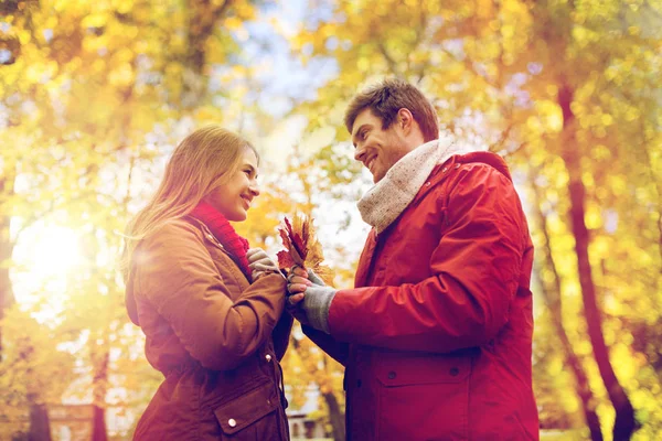 Pareja feliz con hojas de arce en el parque de otoño —  Fotos de Stock