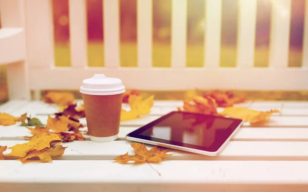 Планшетний ПК і чашка кави на лавці в осінньому парку — стокове фото